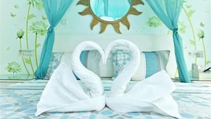 Una cama con una colcha de estampado geométrico, una toalla dispuesta en forma de corazón y un espejo con forma de sol arriba.