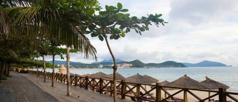 A wooden deck with thatched umbrellas, a beach view, and a wooden fence.