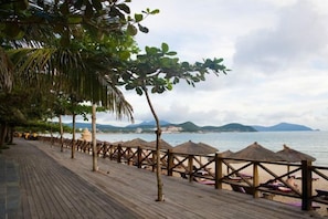 A wooden deck with thatched umbrellas, a beach view, and a wooden fence.