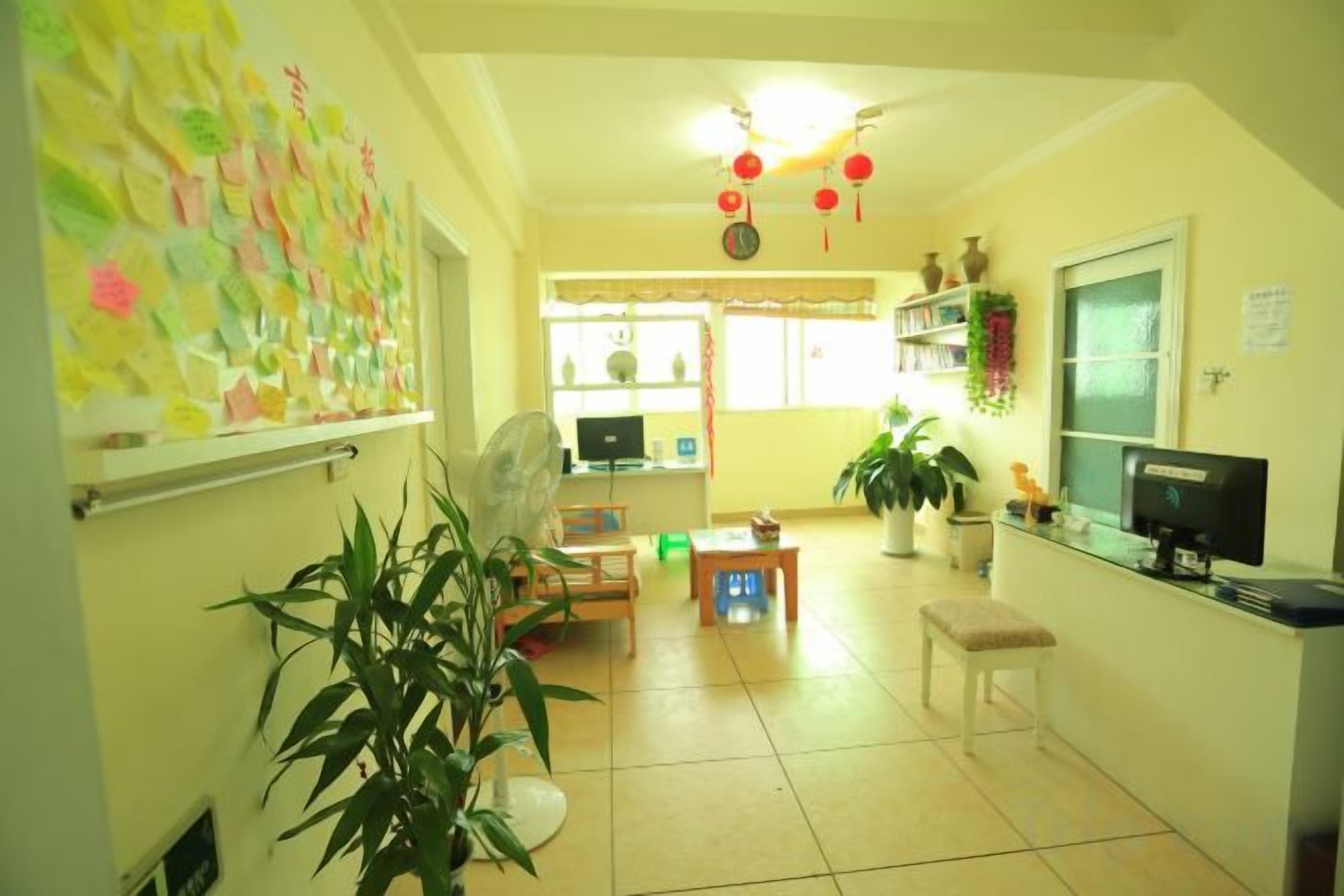 Una habitación con escritorio, silla, ventilador, plantas en macetas y una ventana con cortinas.