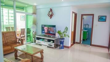 Una sala de estar con televisor, muebles de madera, una planta en maceta y un ventanal corredizo que da a un balcón.