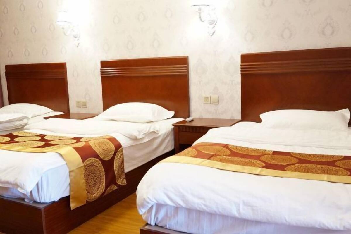 A hotel room with two beds, each with a wooden headboard, white bedding, and a patterned throw.