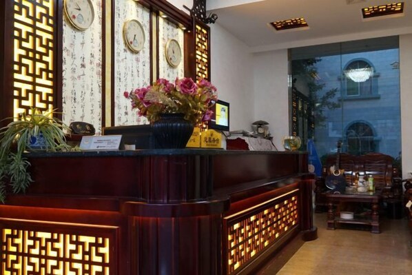 A reception desk with a clock, a vase with flowers, and a computer monitor. - Shiping Jinbi Hotel (Shiping)