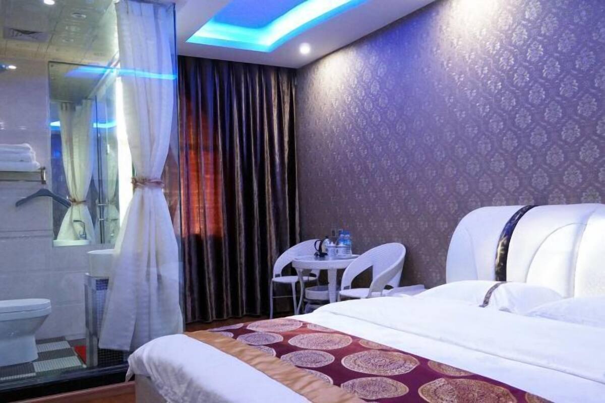 A hotel room with a bed, a small table with chairs, a bathroom with a toilet, and a shower area.