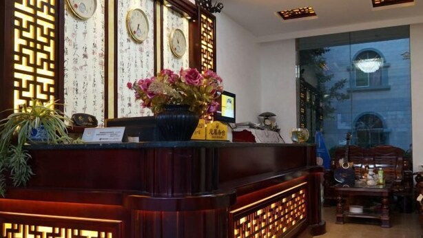Un mostrador de recepción con detalles de madera oscura, un jarrón de flores rosadas y relojes de pared tradicionales.