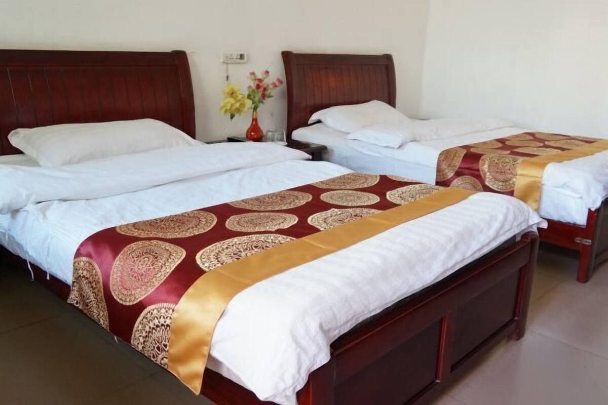 Two single beds with wooden headboards, white linens, and a red and gold patterned bedspread.
