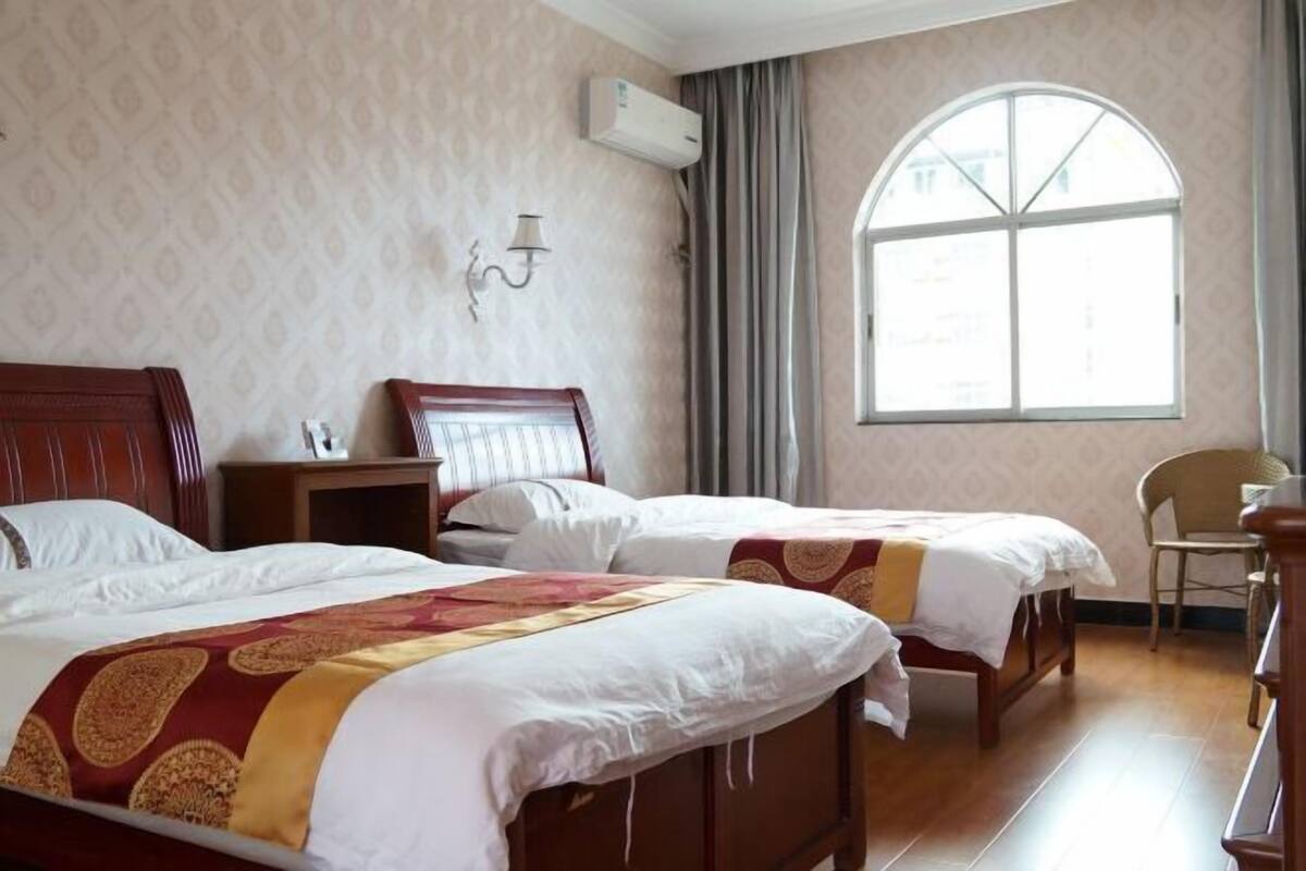 A hotel room with two beds, a nightstand, a chair, a window with a view, and an air conditioning unit.