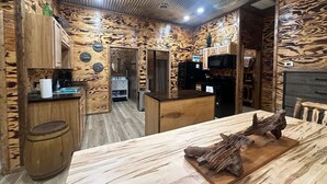 Een rustiek houten interieur met een centrale eettafel, houten kasten en een keukenhoek.