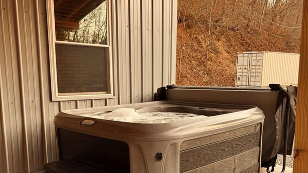 Een hottub met een houten terras, een raam en een metalen bak op de achtergrond.
