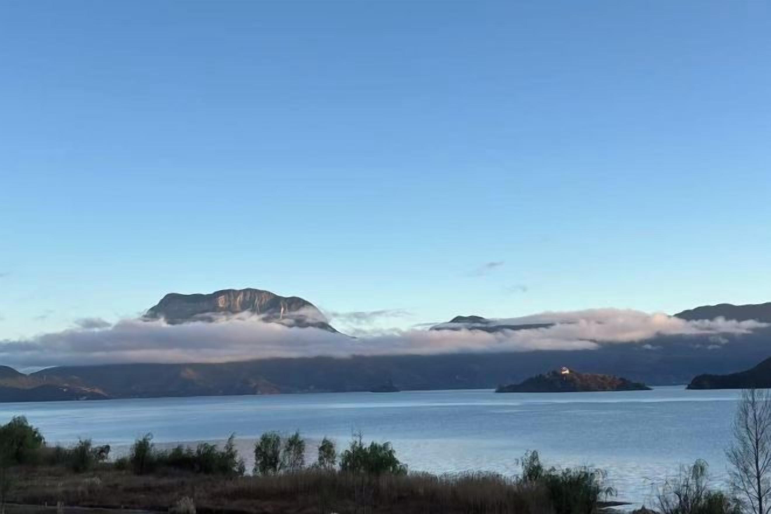 A calm lake with mountains in the background and a small island with a lighthouse.