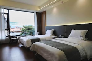 Ein Hotelzimmer mit zwei Betten, einem großen Fenster und Blick auf die Stadt.