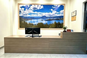 Un mostrador de recepción con un monitor de computadora, un cuadro enmarco con un paisaje y una pequeña planta en maceta.