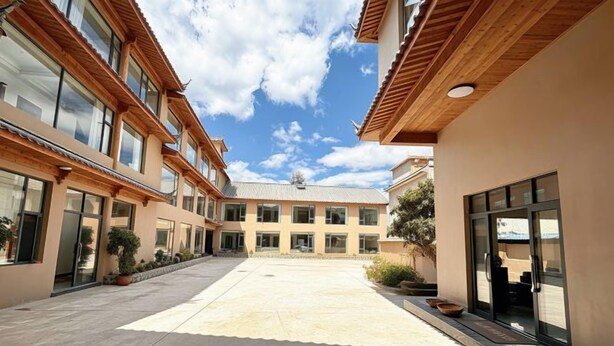 A courtyard with a central open space surrounded by buildings with large windows and wooden beams. - Lugu Lake Yongzhen Hotel (Ninglang)