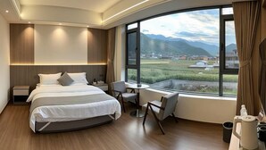 A modern hotel room with a large bed, bedside tables, a desk, and a view of mountains. - Lugu Lake Yongzhen Hotel (Ninglang)
