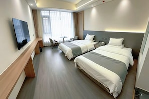 Ein Hotelzimmer mit zwei Betten, einem Fernseher, einem Schreibtisch und einem Fenster mit Vorhängen.