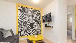 A living room with a zebra print wall, a sofa, a yellow coffee table, and a TV on the wall. - Zebra House Oasis, Ultimate Ft. Lauderdale Studio (Oakland Park)
