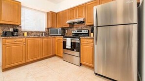 A kitchen with wooden cabinets, a stainless steel refrigerator, a microwave, and a stove. - Zebra House Oasis, Ultimate Ft. Lauderdale Studio (Oakland Park)