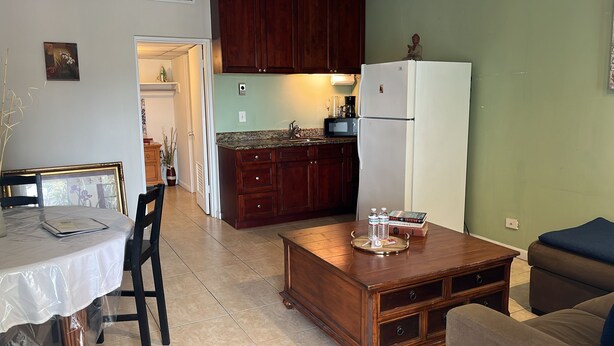A compact kitchen with wooden cabinets, a white refrigerator, and a dining area with a table and chairs. - Relaxed And Spacious Studio 2343
 (Hallandale Beach)