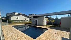 A swimming pool with a tiled deck, a small building with a sign, and a clear blue sky.