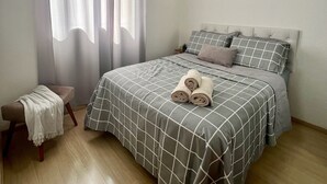 A bedroom with a bed, a bench, and a window with curtains.