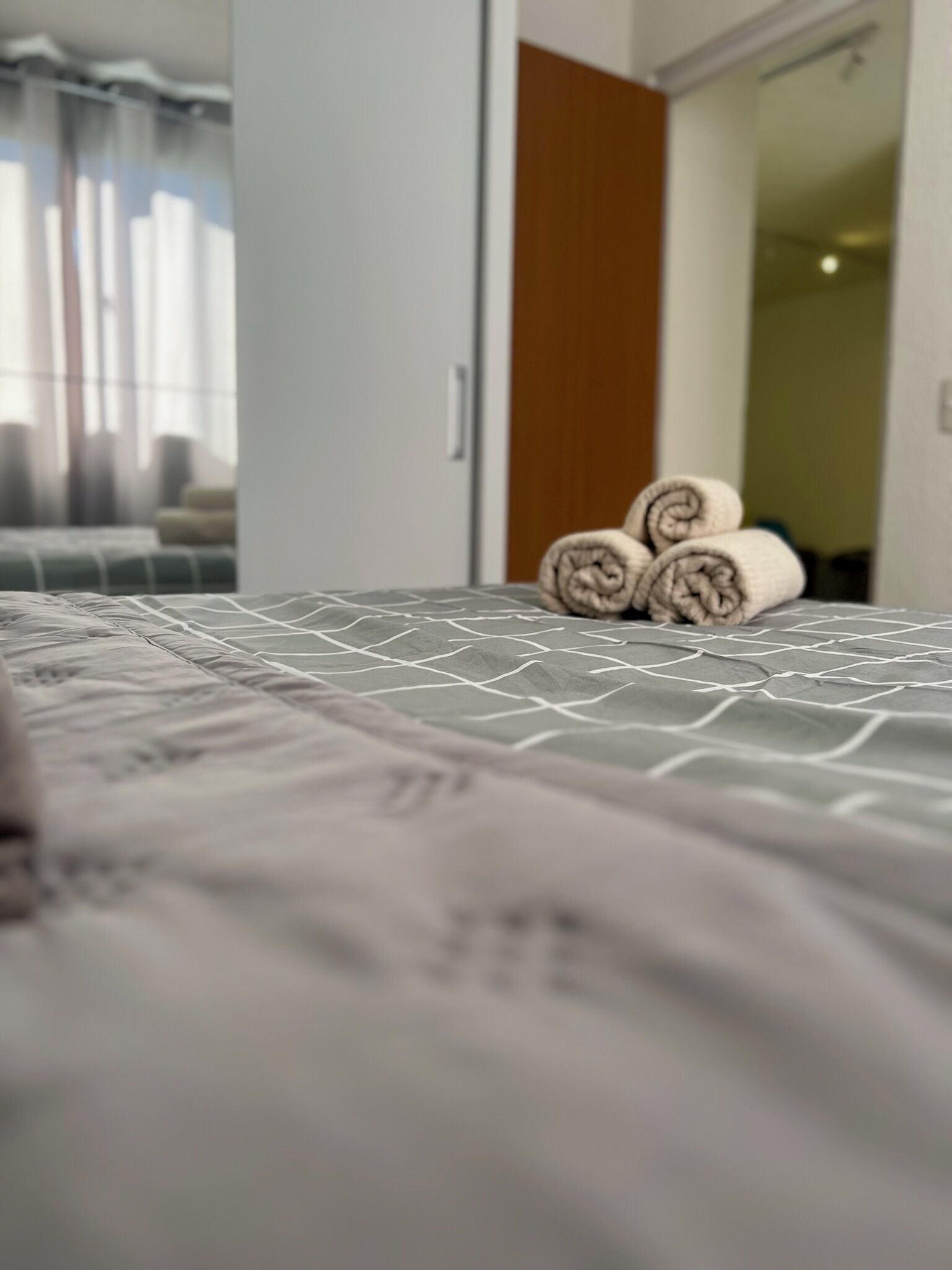 Een net opgemaakt bed met een beddekleed met dessin en opgerolde handdoeken.