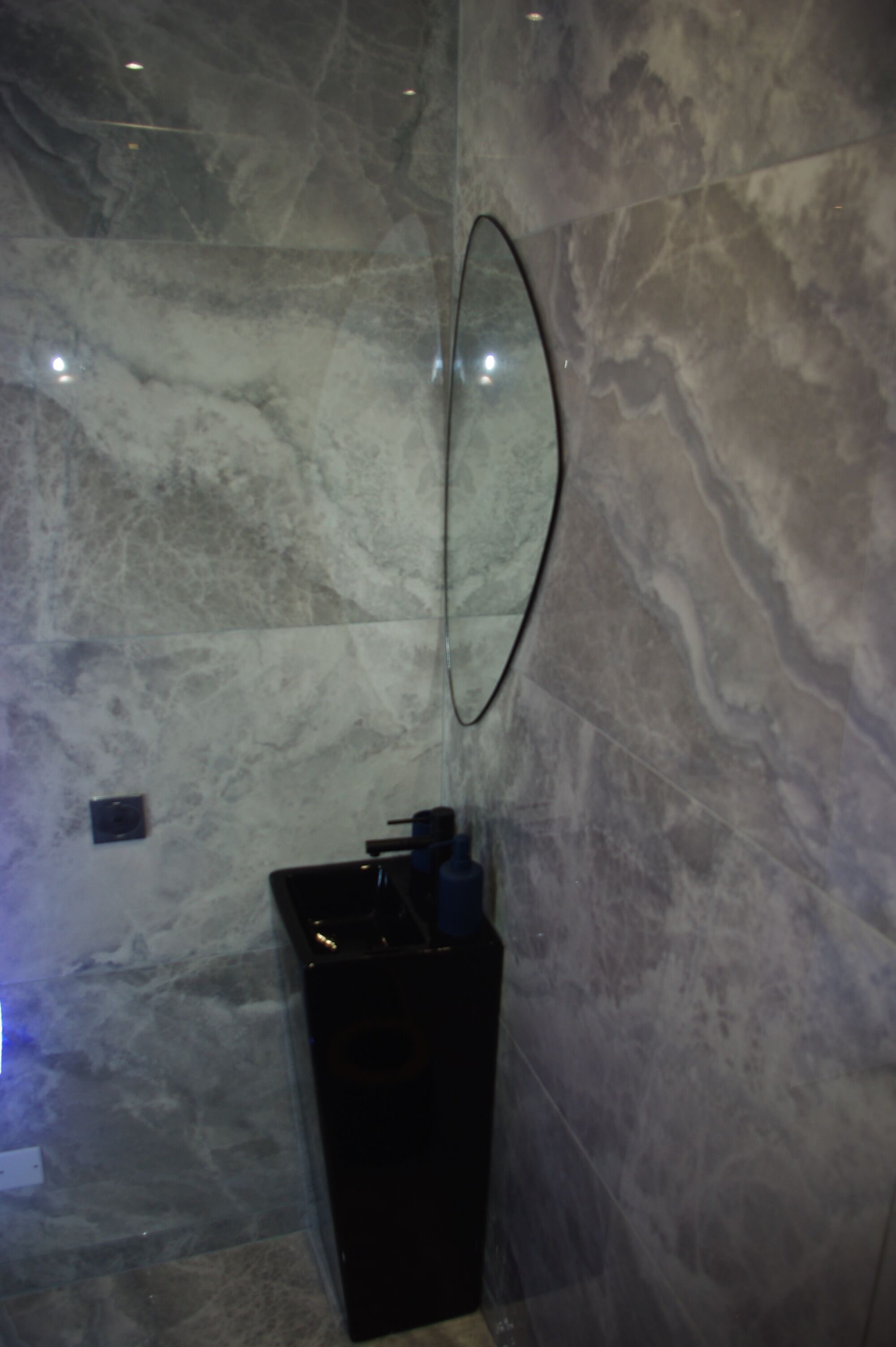 Un bagno con una parete in marmo, un lavandino nero e uno specchio.