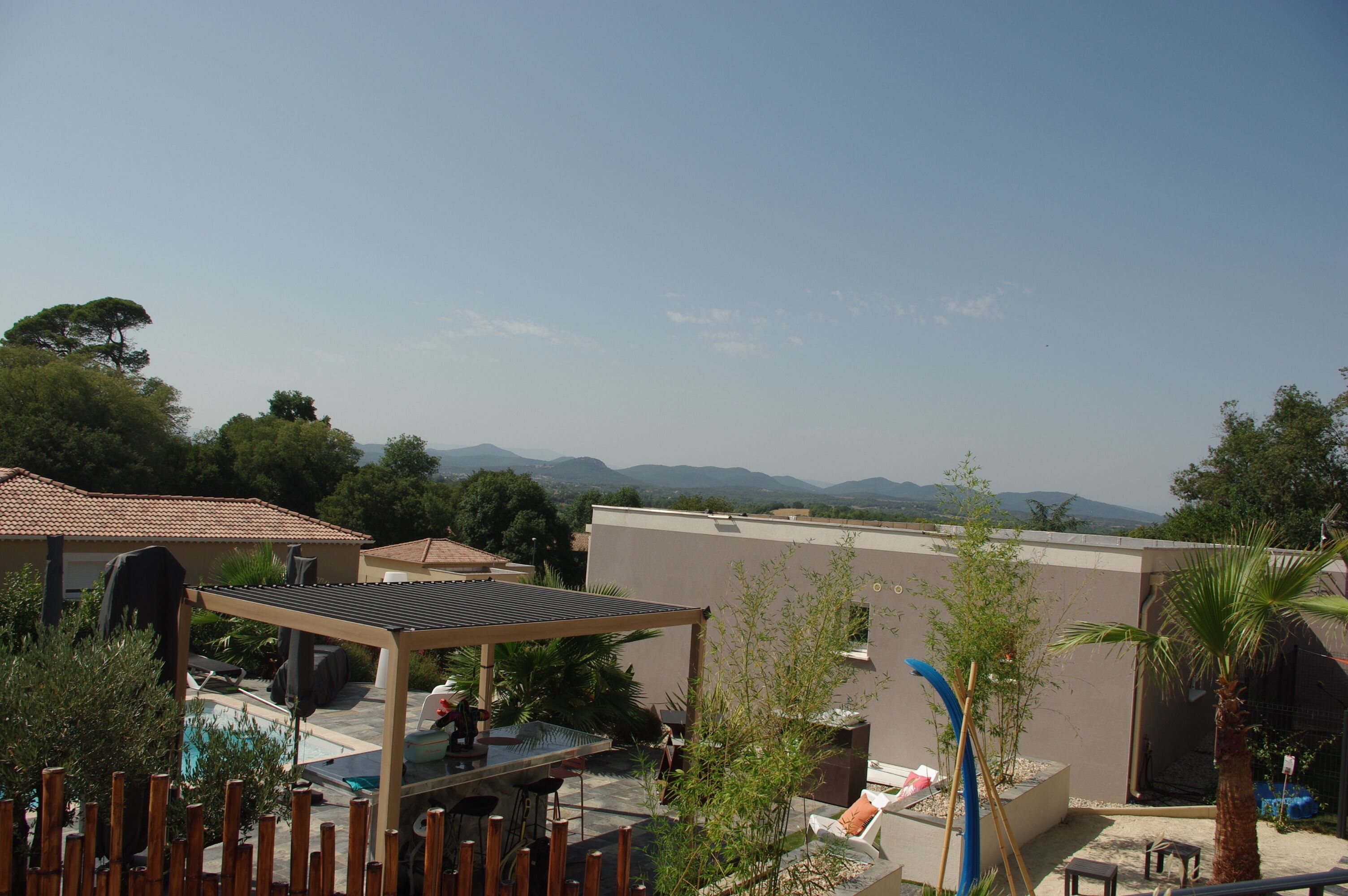 Un espace piscine aménagé sur le toit, avec une pergola, des chaises longues et une vue sur les montagnes lointaines.