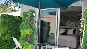 Un espace extérieur moderne aménagé avec des sièges, et une porte vitrée donnant accès à une chambre équipée d’un lit et d’un canapé.