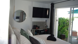 Une chambre d’hôtel moderne équipée d’un lit, d’un bureau, d’un téléviseur à écran plat et d’une porte-fenêtre coulissante donnant sur un balcon agrémenté de plantes.