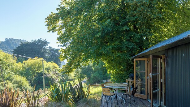 A wooden deck with a table and chairs, surrounded by lush greenery and a large tree. - The Overleigh Shearers Quarters (Port Levy)