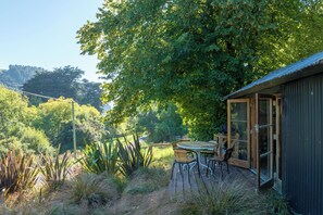 Eine Holzterrasse mit Tisch und Stühlen, umgeben von üppiger Vegetation und einem großen Baum.