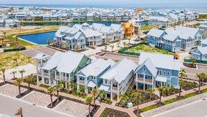 Una zona residencial costera con varias casas de dos pisos, una piscina central y una calle bien cuidada con palmeras.