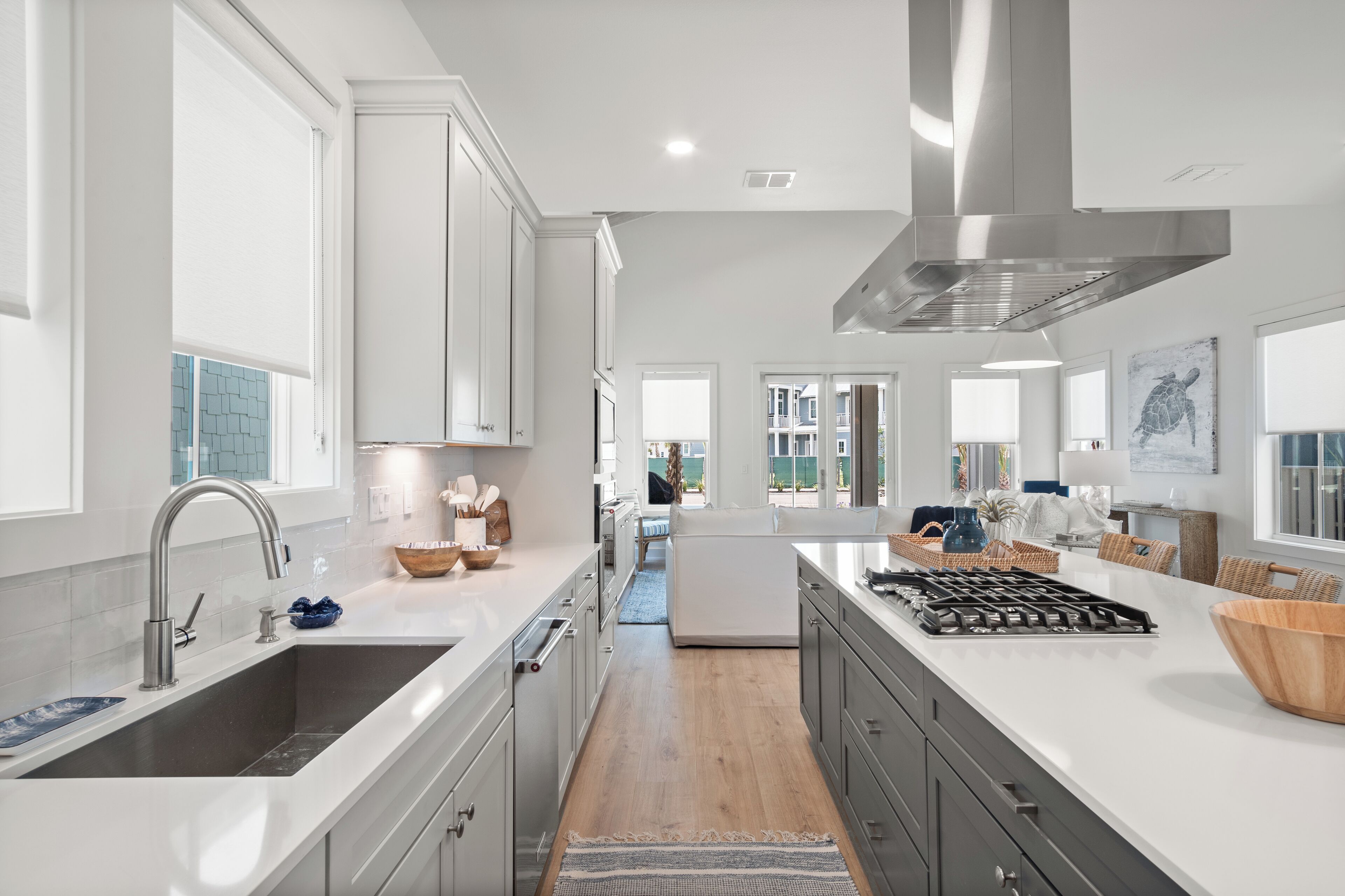 A modern kitchen with white cabinetry, a stainless steel range hood, and a large island with a built-in stove.