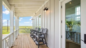 Eine überdachte Veranda mit Holzboden, weißen Geländern und einer Reihe von Stühlen.