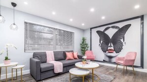 Ein modernes Wohnzimmer mit einem grauen Sofa, rosa Sesseln und einem runden Couchtisch.