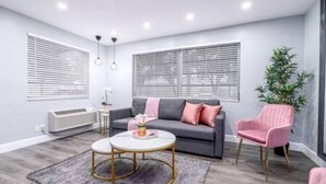 Ein modernes Wohnzimmer mit grauem Sofa, einem runden Couchtisch, einem rosa Sessel und einer Topfpflanze.