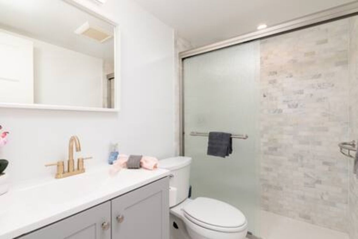 Une salle de bain moderne avec un meuble-lavabo blanc, une douche en verre et des toilettes blanches.