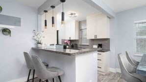 A modern kitchen with a central island, bar stools, pendant lighting, and white cabinetry. - Stylish Vacation home Coral Ridge (Oakland Park)