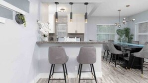 A modern kitchen with a central island, bar stools, pendant lighting, and a dining area with a table and chairs. - Stylish Vacation home Coral Ridge (Oakland Park)