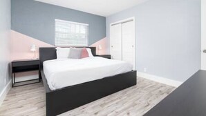A modern bedroom with a bed, bedside tables, and a window. - Stylish Vacation home Coral Ridge (Oakland Park)