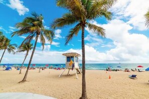 Ein Strand mit Palmen, einem Rettungsturm und Strandsonnenschirmen.