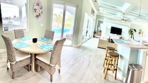 A modern kitchen with white cabinets, a central island, and a dining area with wicker chairs and a round table.