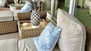 A sunlit indoor seating area with wicker furniture, a pineapple centerpiece, and a view through large glass doors.
