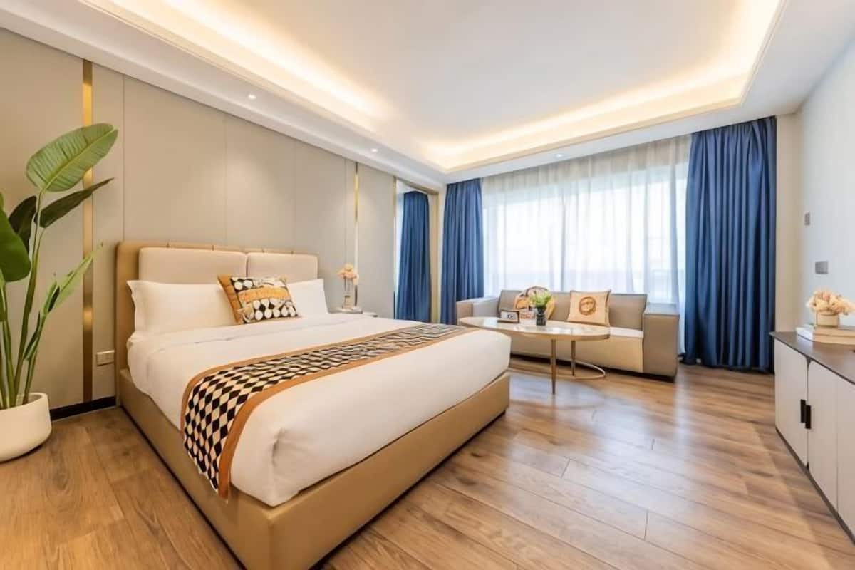 Una habitación de hotel moderna con una cama grande, una mesita de noche, un sofá, un escritorio y una planta en maceta.