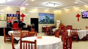 A restaurant with round tables and wooden chairs, a counter with a menu, and a television on the wall. - Jinyuan Hotel (Emeishan City)