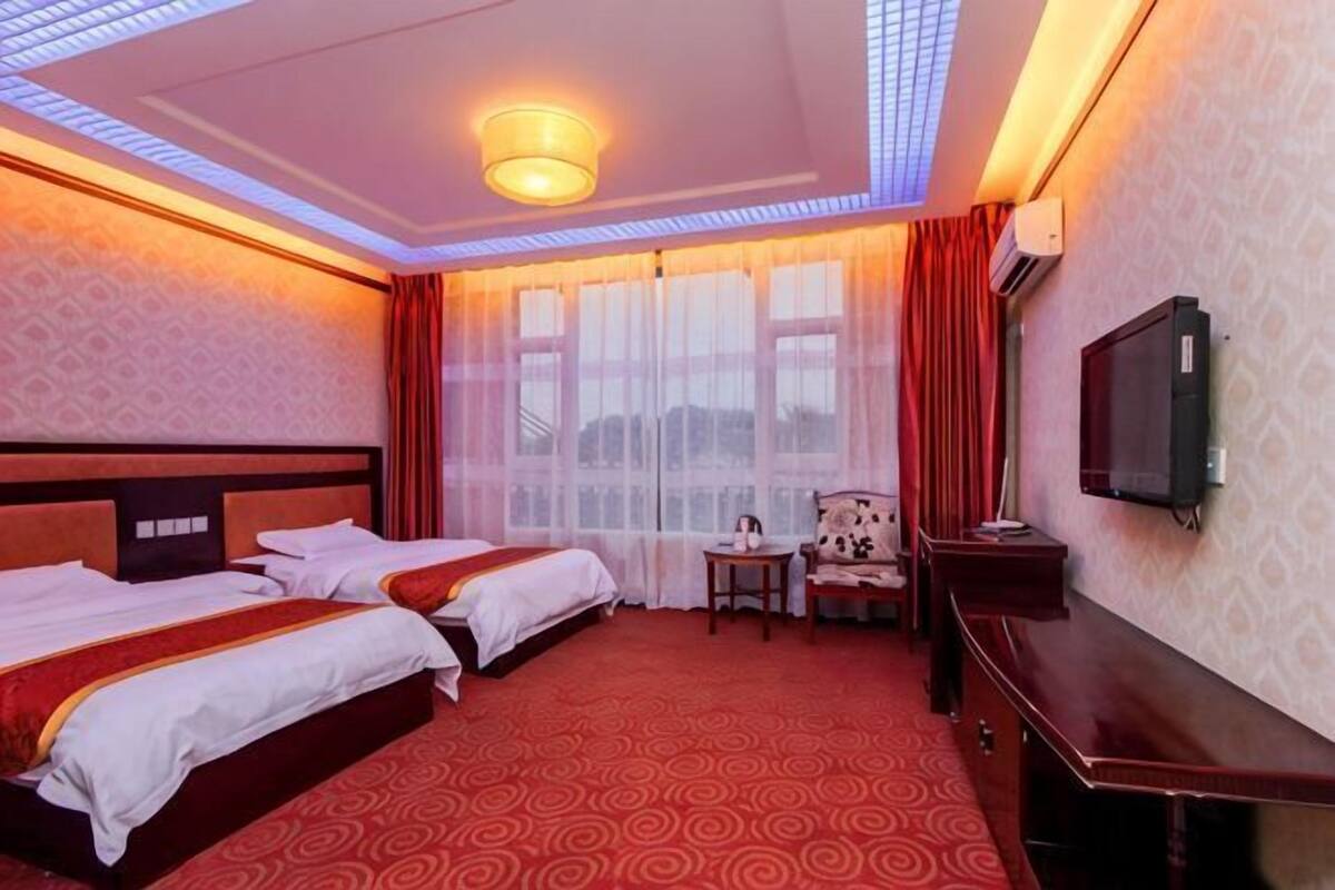 A hotel room with two beds, a TV, a desk, and a chair.