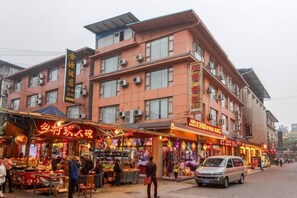A multi-story building with commercial shops on the ground floor, air conditioning units, and a vehicle parked outside. - Jinyuan Hotel (Emeishan City)