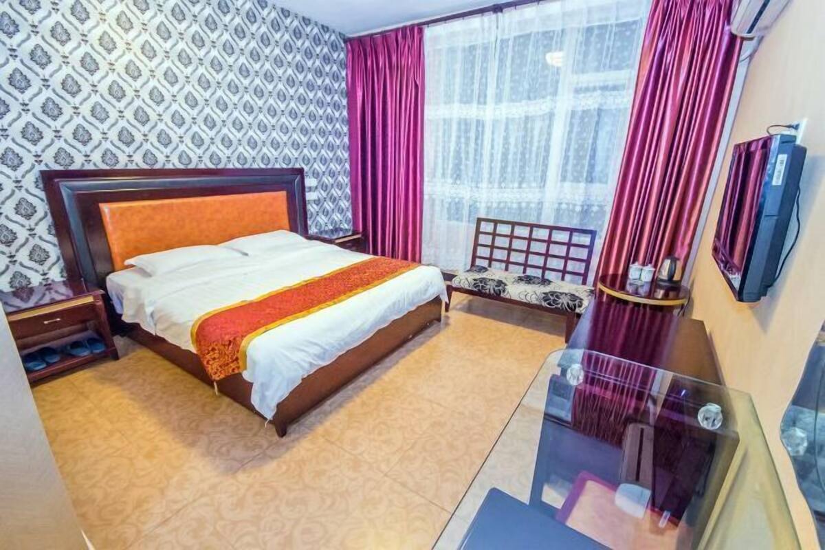 A hotel room with a bed, a small seating area, a TV, and a window with curtains.