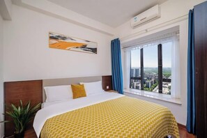 A hotel room with a bed, a window with curtains, a plant, and a painting on the wall. - Angda Pazhou Apartment (Guangzhou Pazhou International Exhibition Center) (Guangzhou)