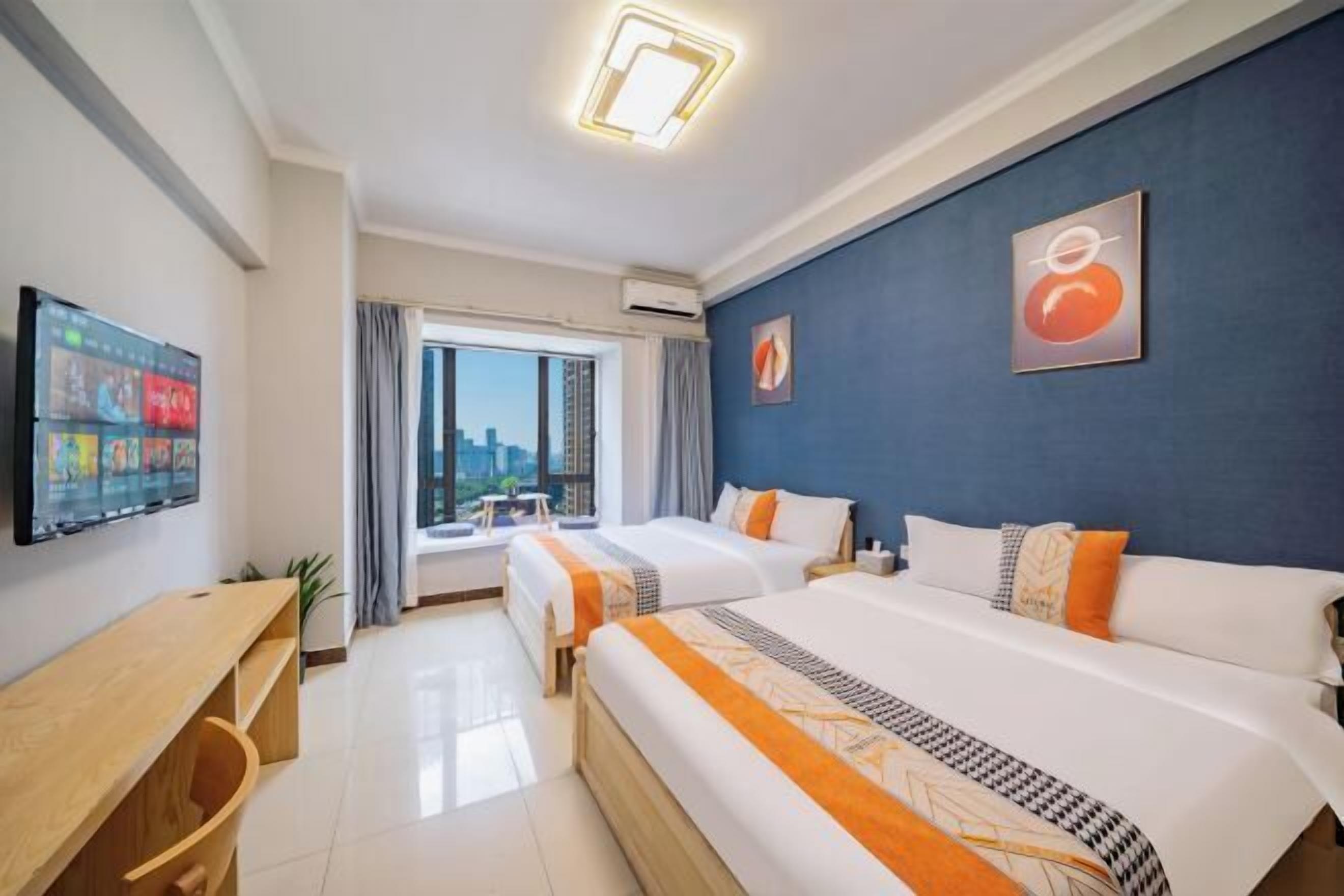 Habitación de hotel con dos camas, televisión, escritorio y ventana con vistas a la ciudad.